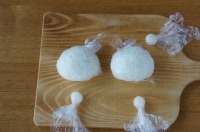 ラップに塩を薄くふり、50gのご飯をのせて顔の形に握ります。これを2つ作ります。残りの少量のご飯は3等分に分けて、それぞれラップで丸く形を整えます。<br />