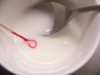 爪楊枝の先で、ピンクの着色料をすくい取って加えて、よく混ぜる。<br />